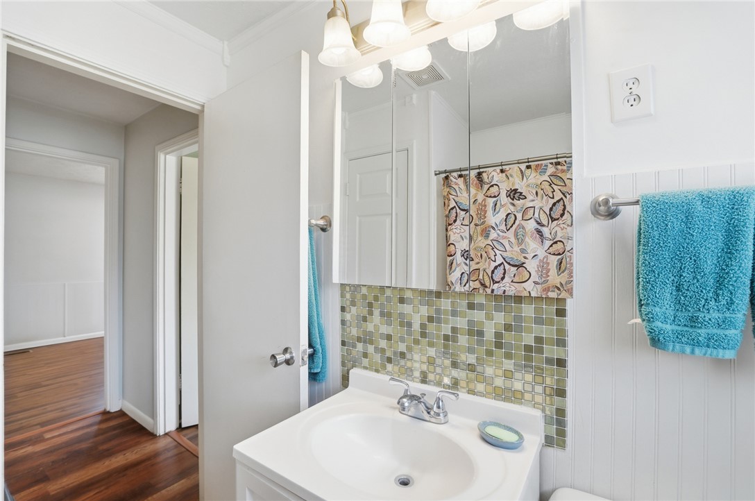 Bathroom vanity with a green mosaic tile backsplash, mirrored cabinet, and patterned shower curtain.