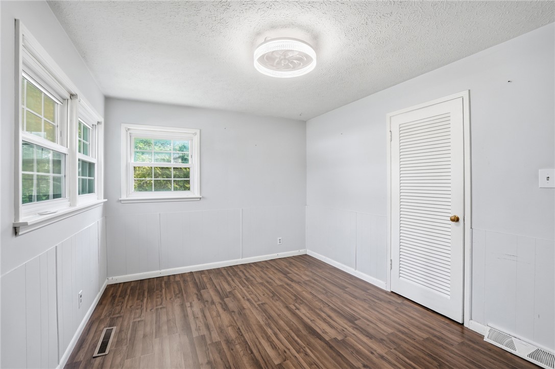 Empty room with wood-look flooring, paneled walls, several windows, and a louvered closet door.