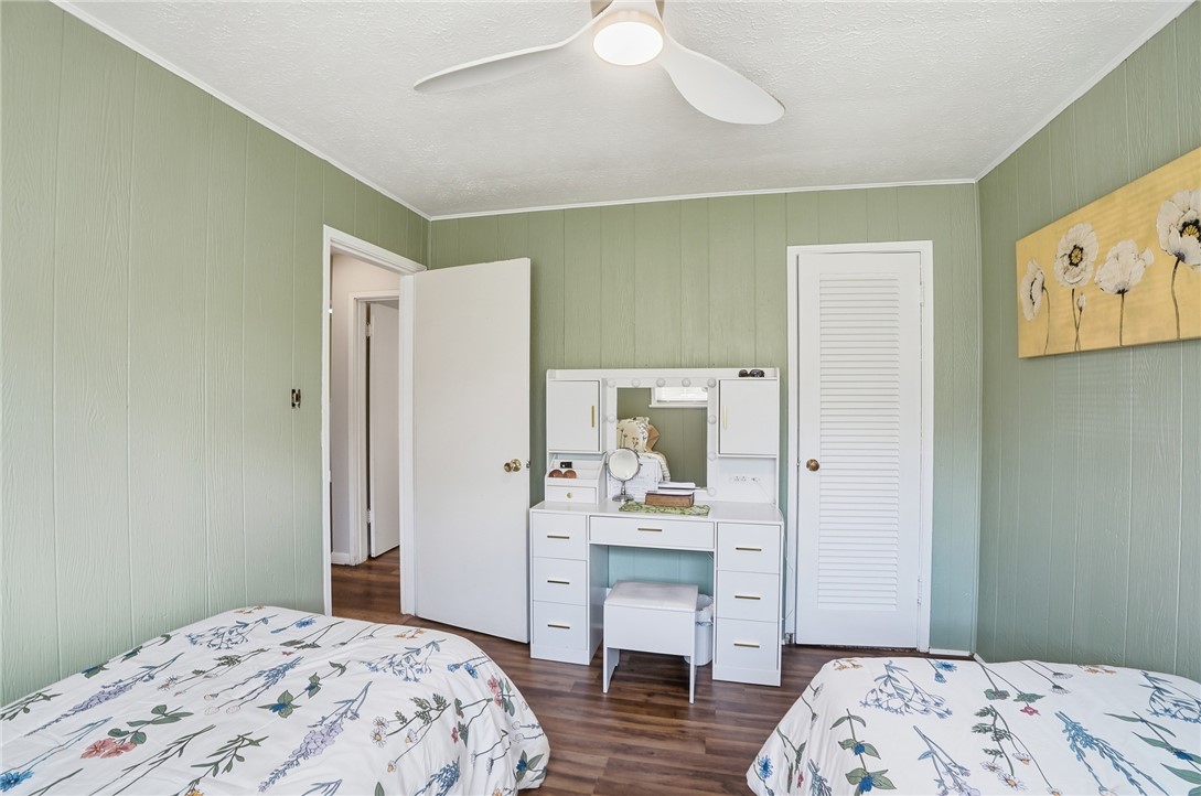 Bedroom with sage-green paneled walls, floral bedding, a white vanity, and wood-look flooring.
