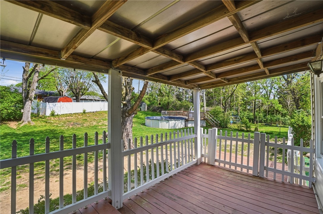 Covered rear deck with white railings overlooking a tree-lined backyard and above-ground pool.