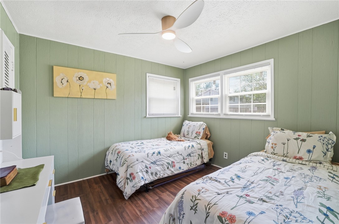 Bedroom with two floral-covered beds, pale green walls, and windows with white blinds.