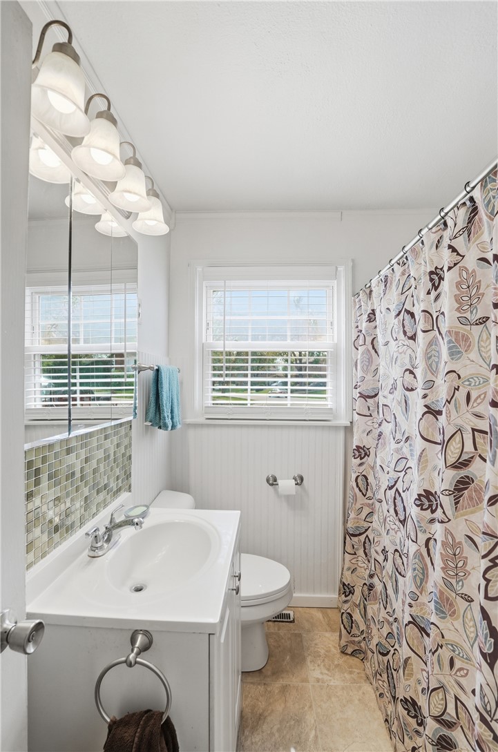 Compact bathroom with a white vanity, green tile accents, and a patterned shower curtain.