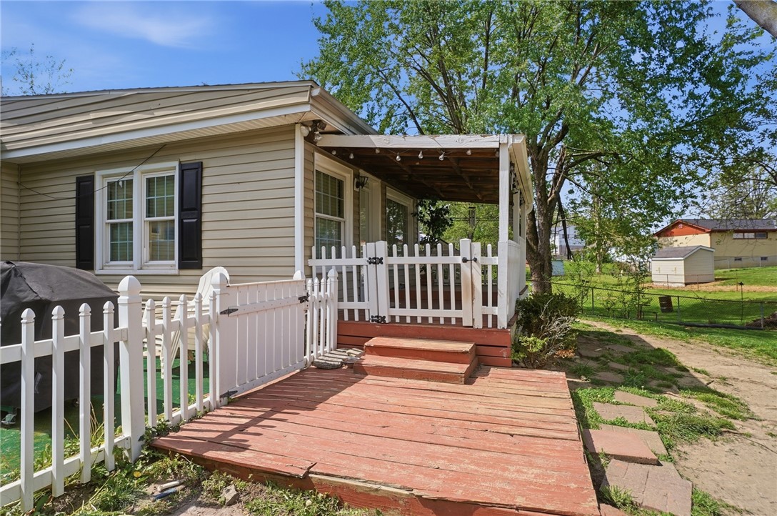 Home’s rear deck and covered porch with white picket fencing and a grassy yard.