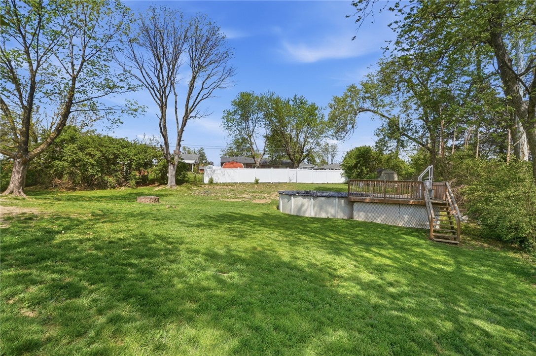 Backyard with a grassy lawn, mature trees, and an above-ground pool surrounded by a wooden deck.