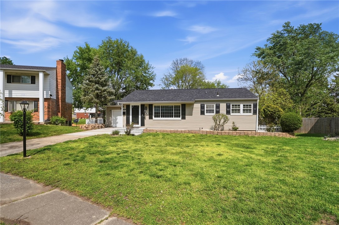 Single-story ranch house with light siding and dark shutters behind a broad green lawn.