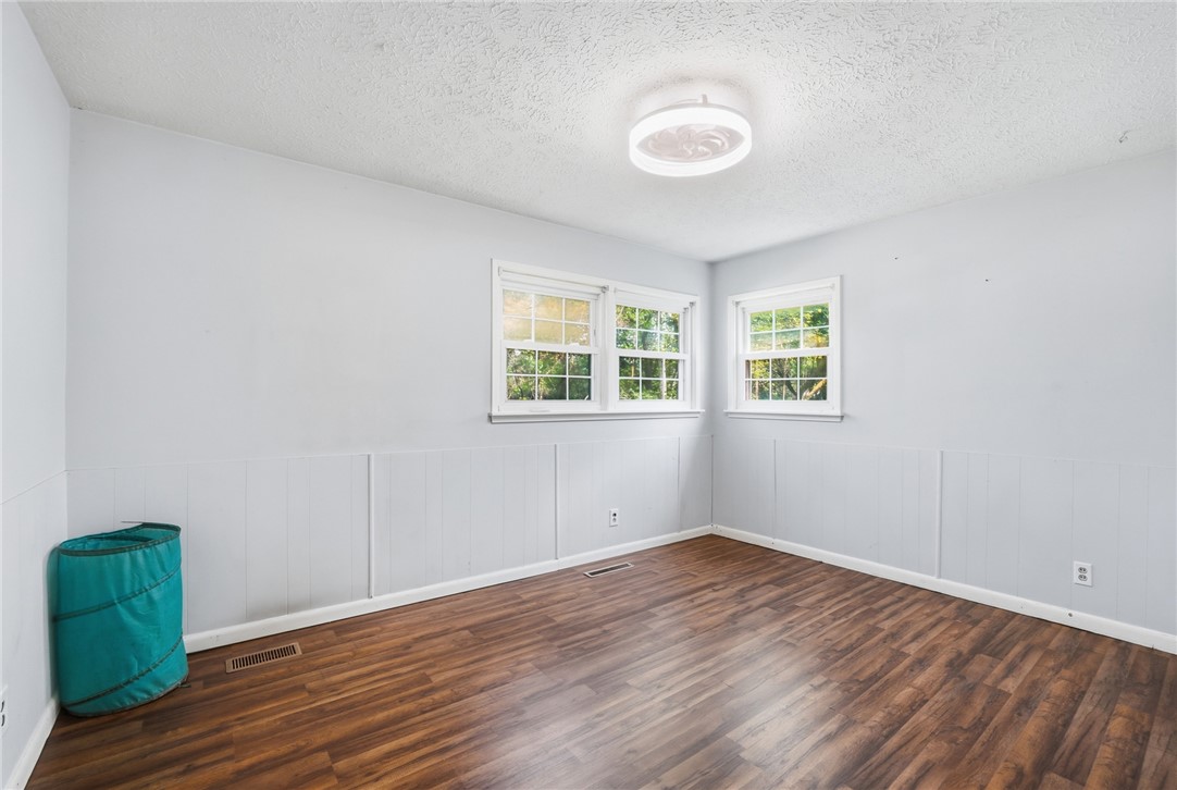Empty room with brown wood-look flooring, white wainscoting, and three windows.