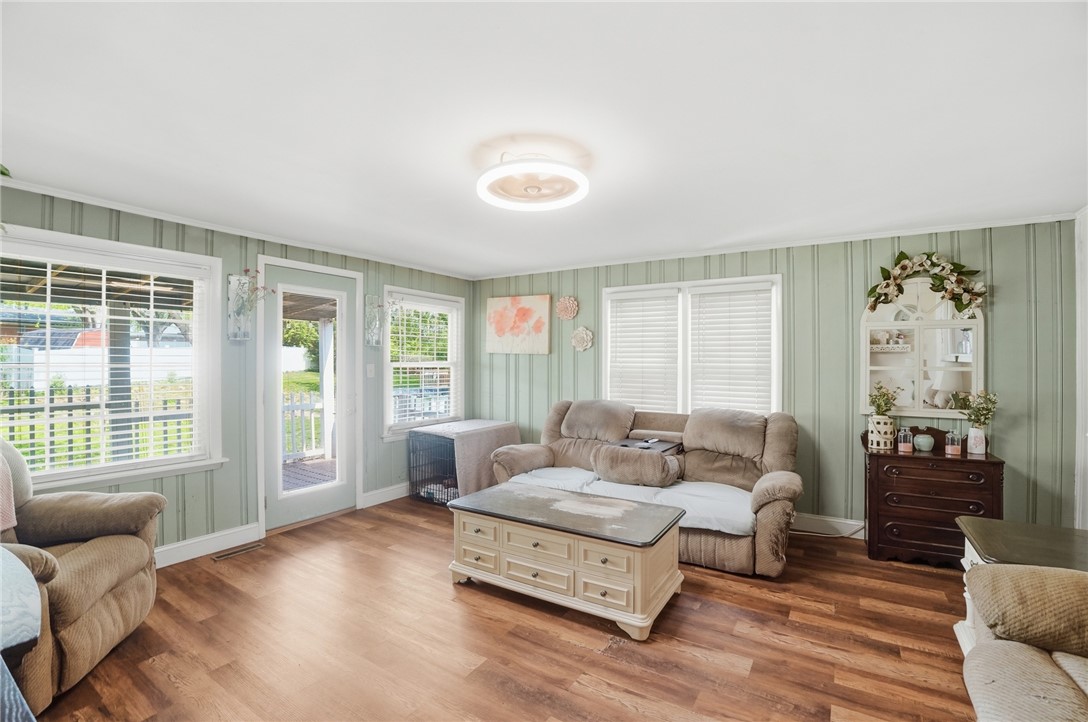 Living room with pale green striped walls, wood floors, and beige seating beside bright windows.