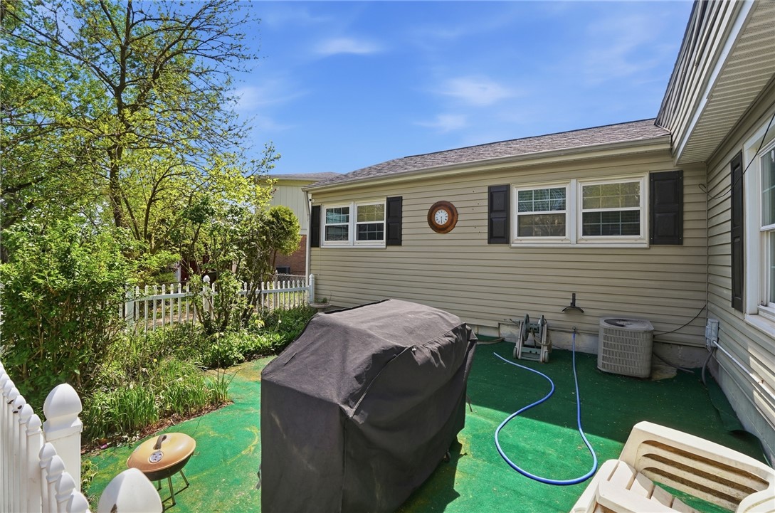 Fenced patio beside a beige-sided home, with artificial turf and a covered grill.