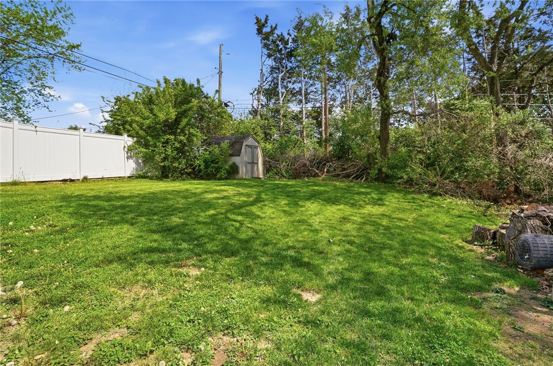 Backyard with a broad lawn, white privacy fence, small shed, and mature trees.