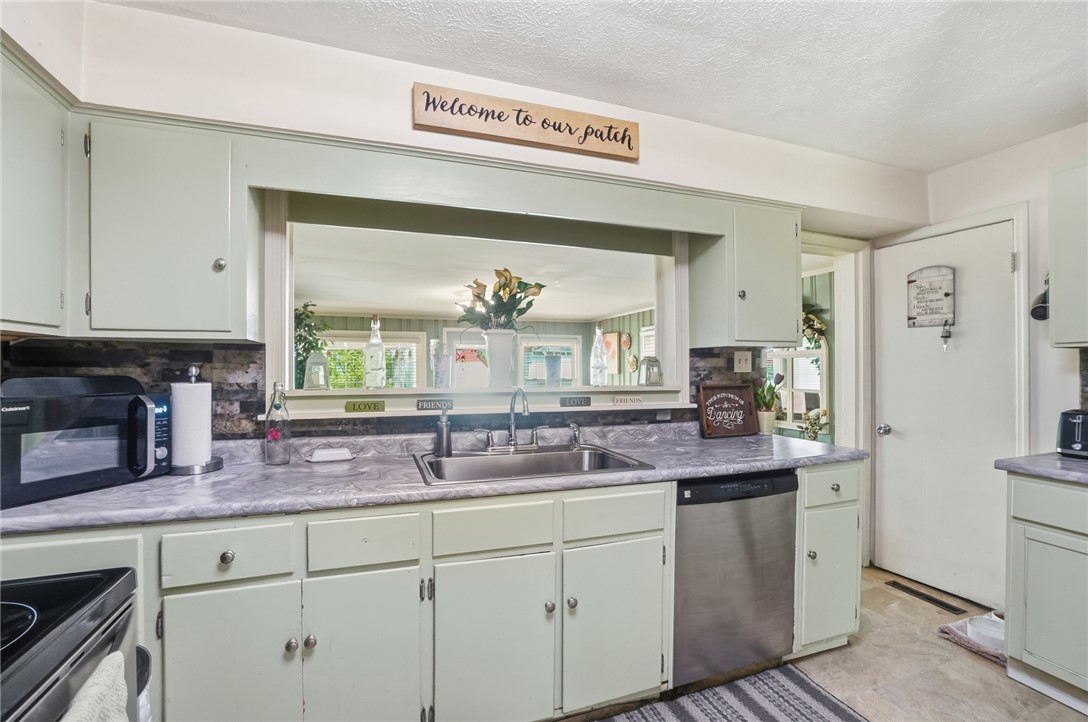 Kitchen with pale green cabinets, a wide pass-through opening, and a stainless-steel dishwasher.