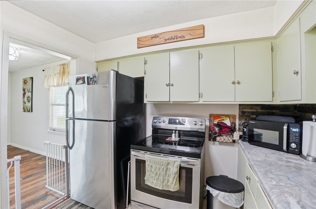 Kitchen with pale green cabinets, stainless-steel appliances, and a marble-look countertop.