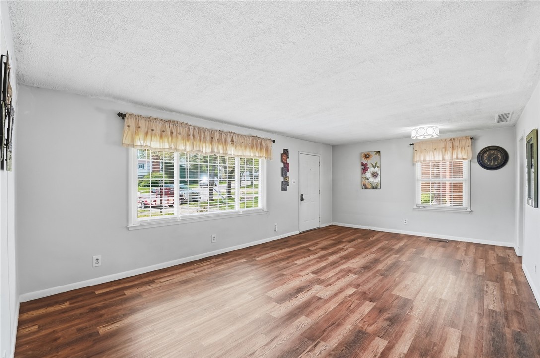 Empty living room with wood-look floors, two windows, and white walls.