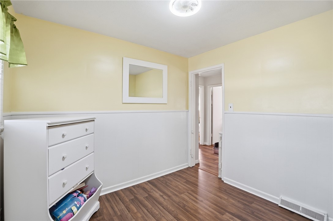 Bedroom with yellow walls, white wainscoting, wood-look flooring, and a white dresser