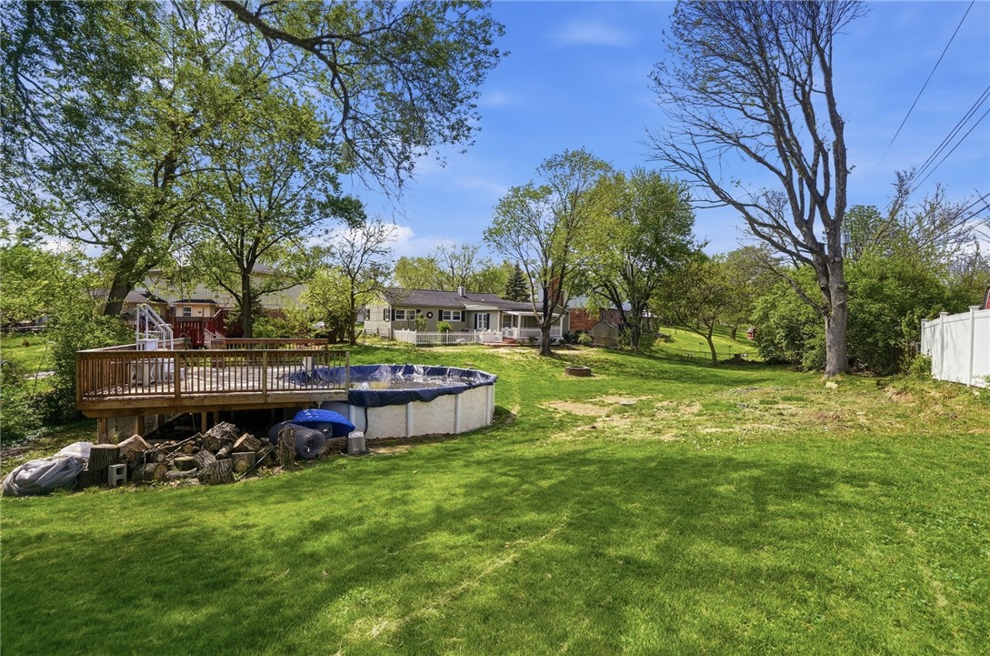 Backyard with a broad lawn, mature trees, raised deck, and above-ground pool.
