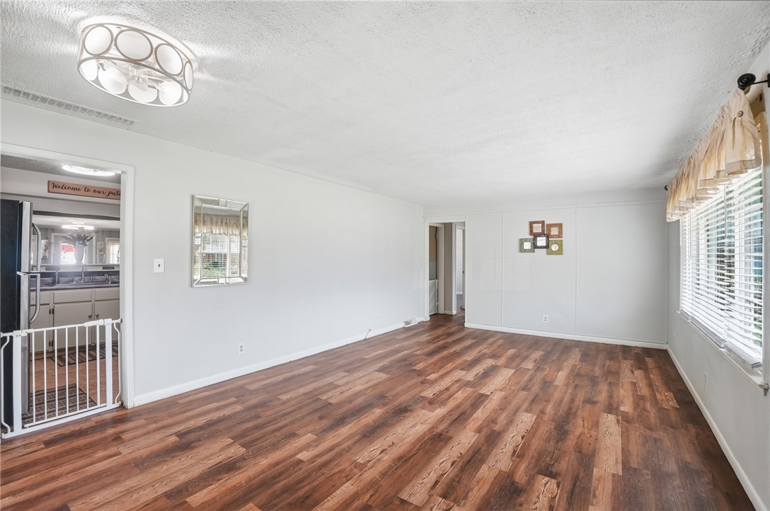 Empty living room with wood-look flooring, a large window, and an opening to the kitchen.