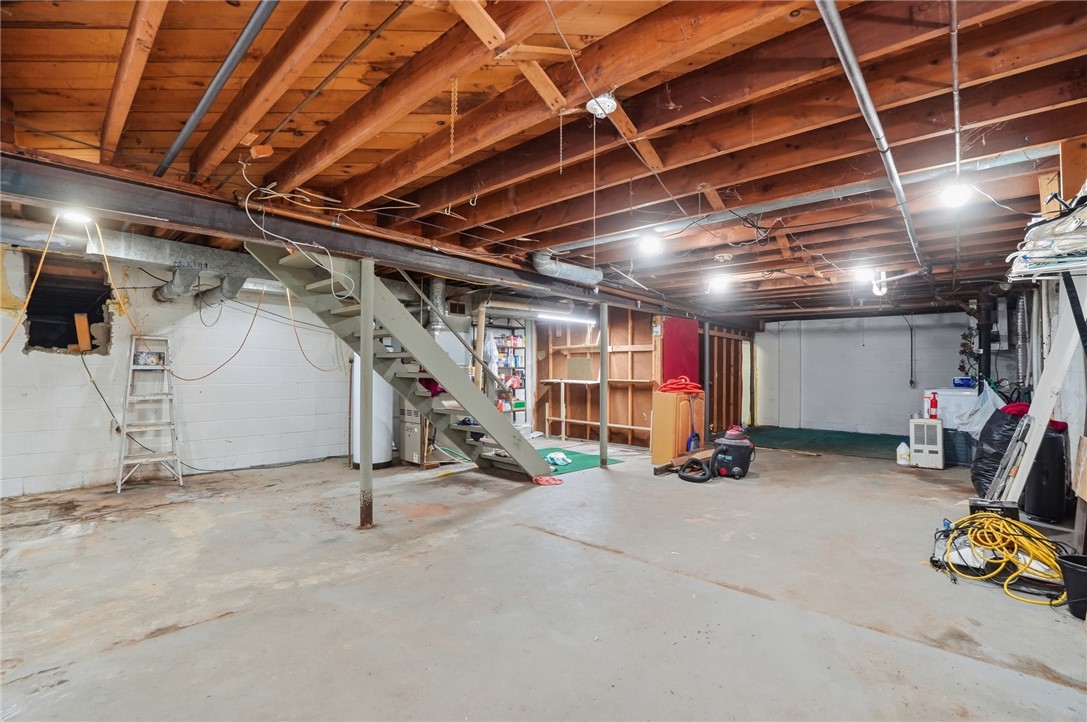 Unfinished basement with exposed joists, a concrete floor, and stairs to the upper level.