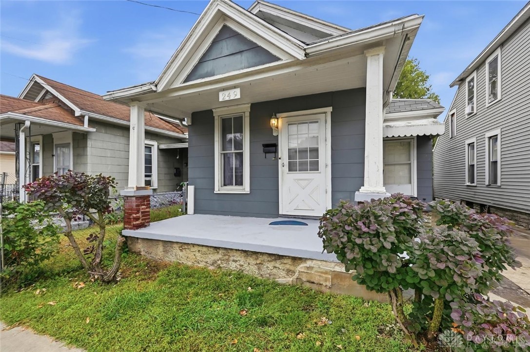 Blue-gray house with a white covered porch, front shrubs, and number 249 above the entrance.