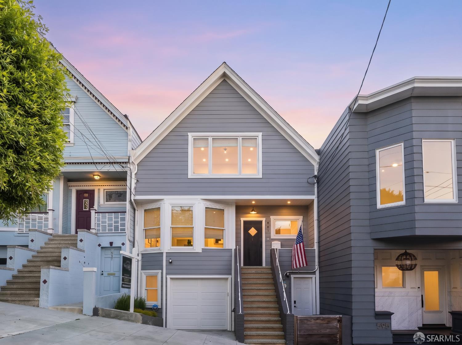 Gray gabled home with a white garage, front steps, and an American flag at dusk.