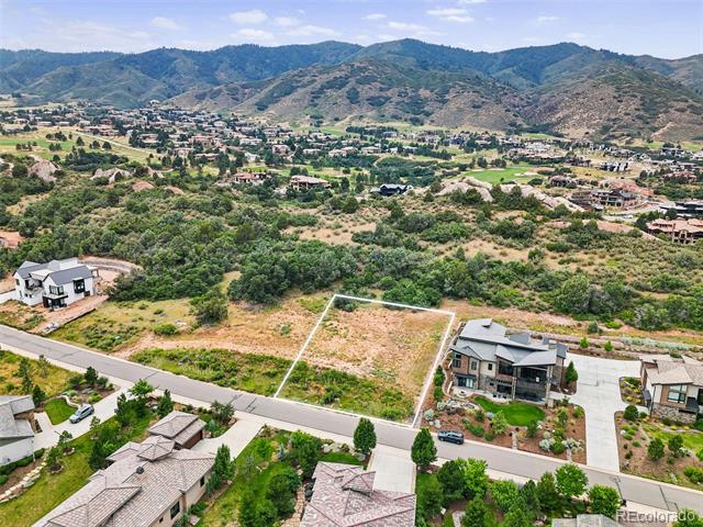 Vacant residential lot outlined in white, with nearby homes and mountain foothills in the distance.
