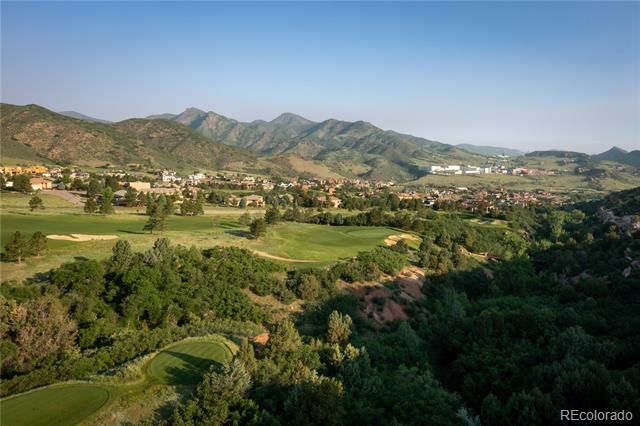 Aerial view of a golf course and homes below green Colorado foothills.