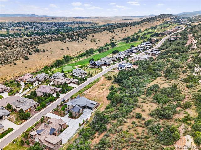 Aerial view of hillside homes along a winding road beside a broad green corridor.