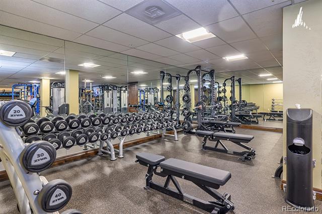 Fitness room with mirrored walls, rows of dumbbells, weight machines, and workout benches.