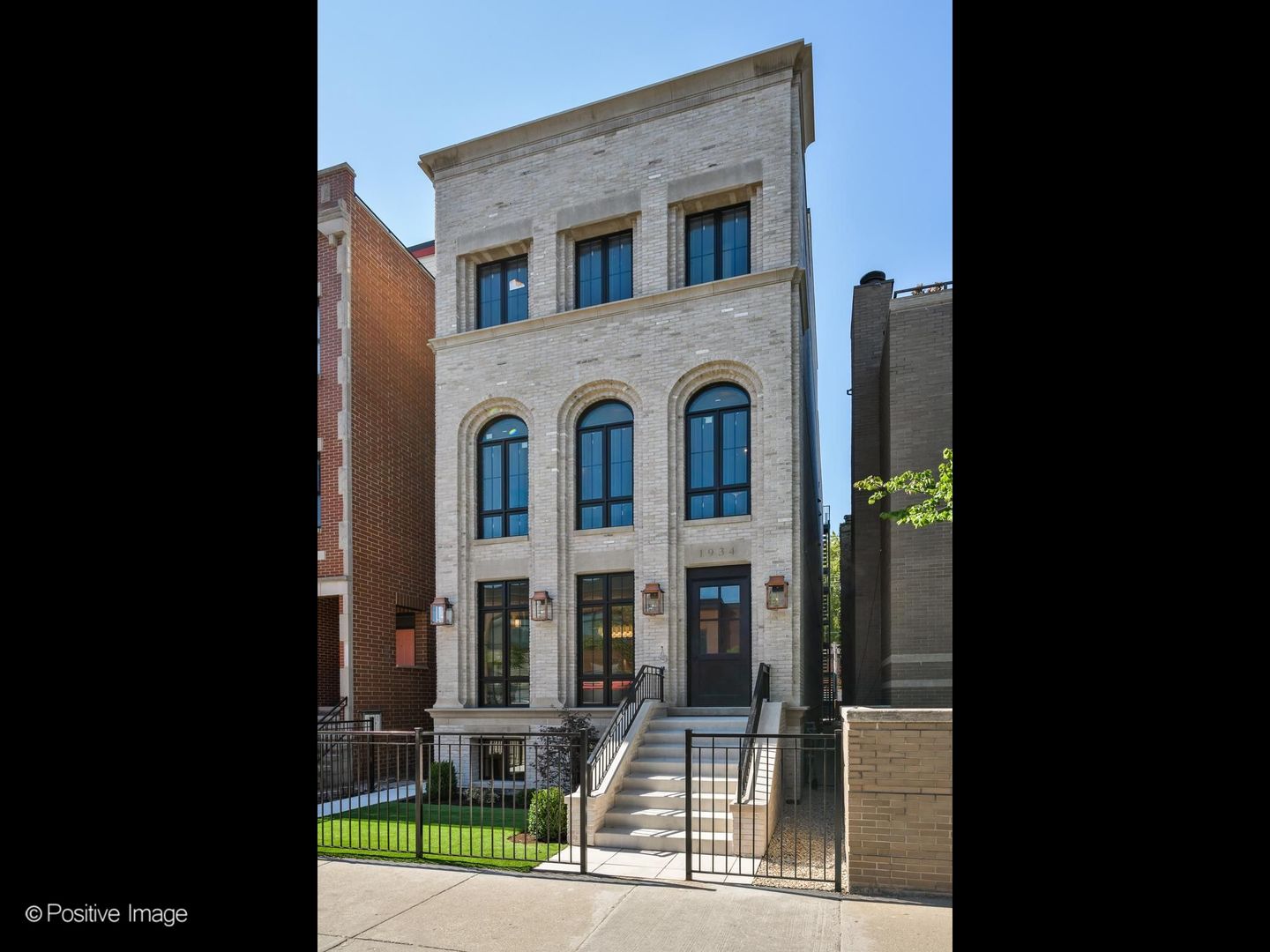 White-brick residence with arched windows, a raised front staircase, and fenced garden.