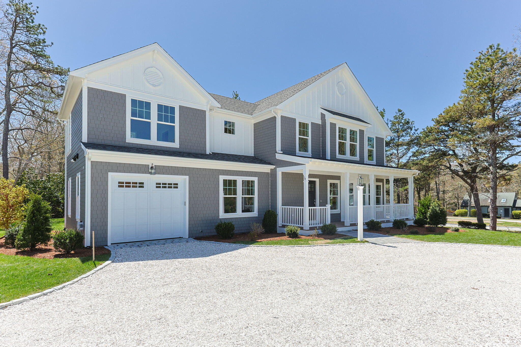 Gray-shingled two-story house with a white covered porch and broad gravel driveway.