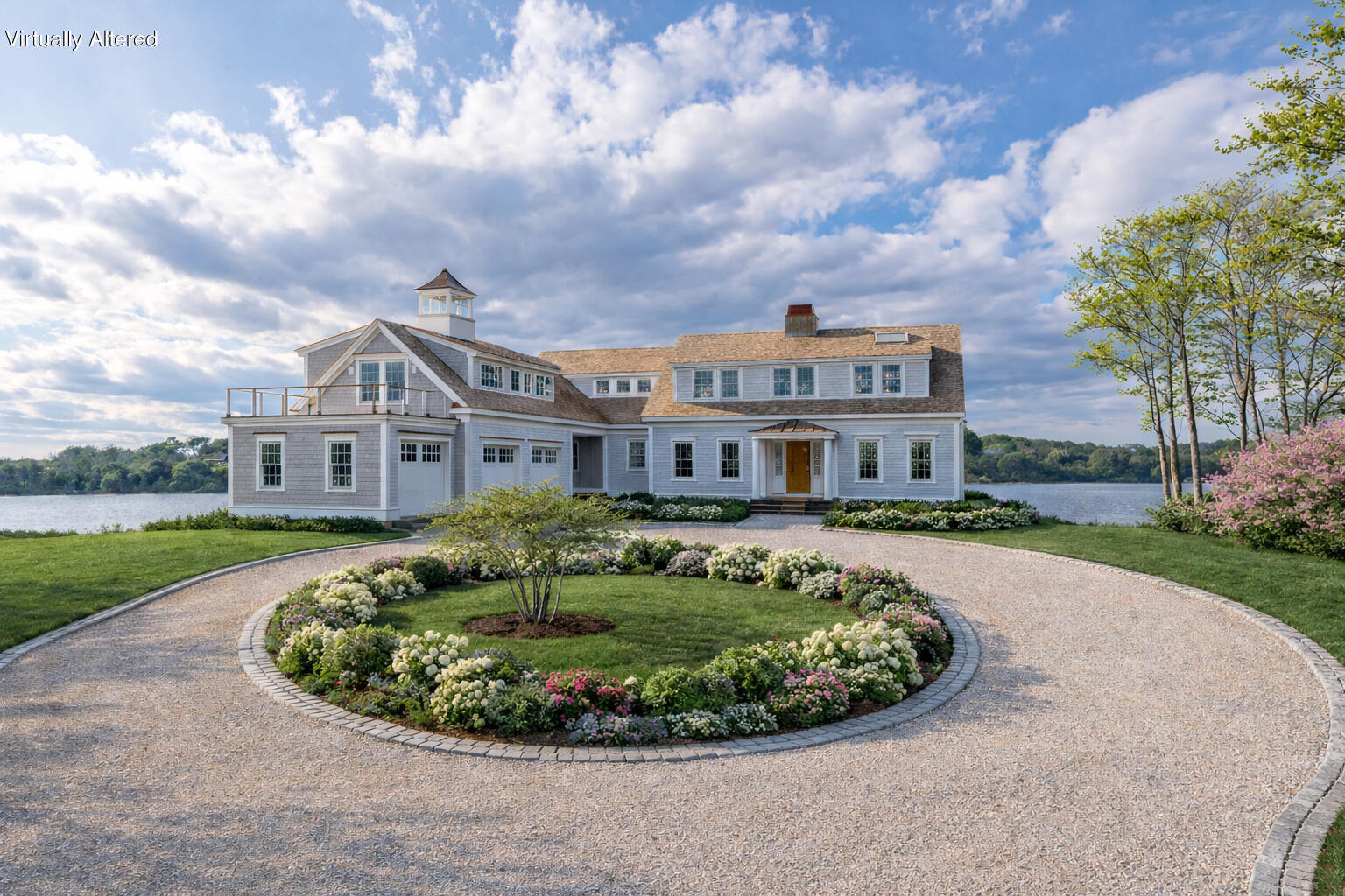 Waterfront shingle-style home with a circular gravel drive and flower garden.