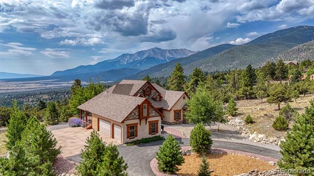 Mountain home with a broad driveway and pine trees, backed by a sweeping mountain landscape.