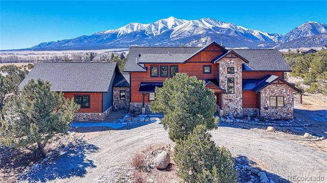 Mountain home with red siding and stone accents, backed by snow-covered peaks.