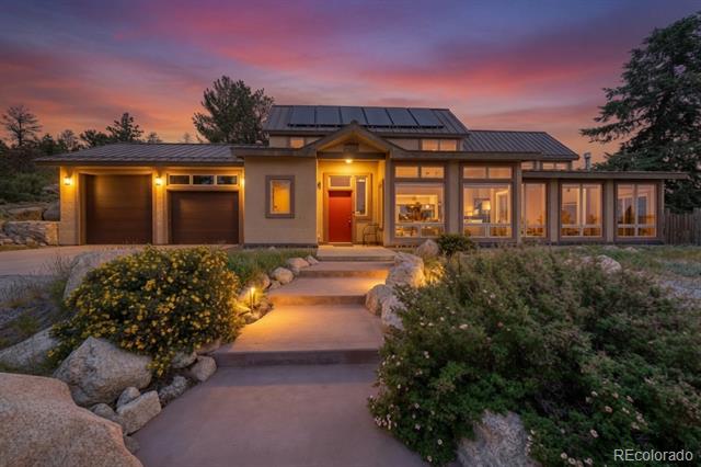 Modern single-story home with solar panels, a double garage, and a stone garden path at dusk.