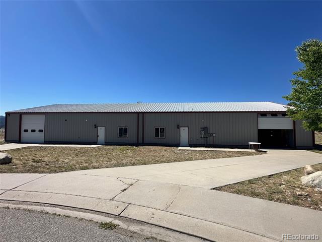Long gray commercial building with a large open bay and concrete driveway.