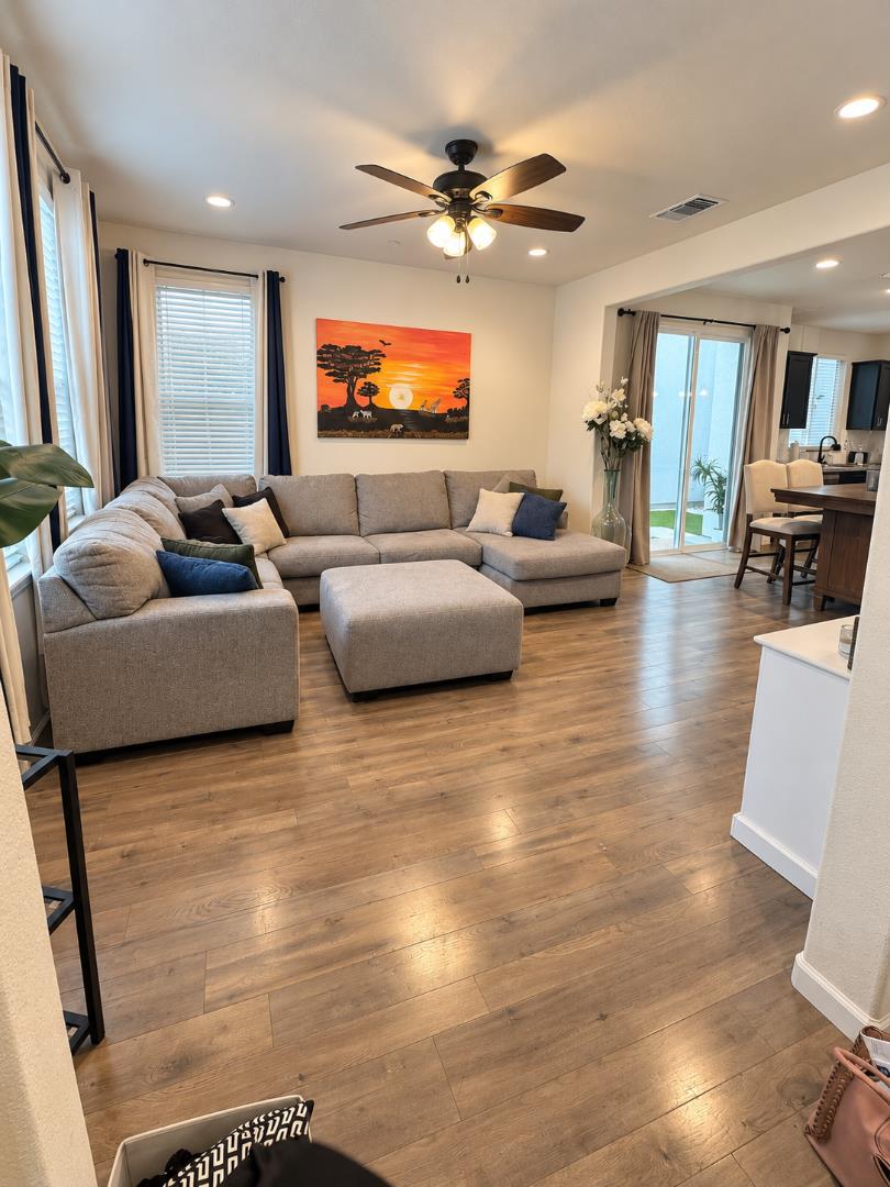 Furnished living room with a gray sectional, wood floors, ceiling fan, and sliding glass doors.
