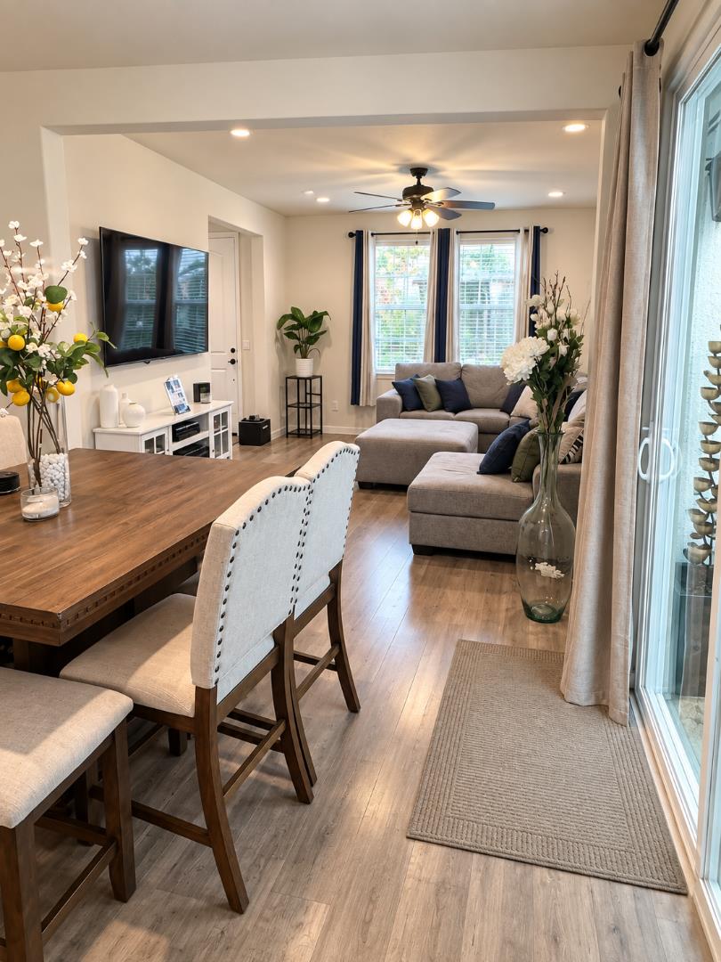 Open-plan living and dining room with a gray sectional, wooden table, and sliding glass doors.
