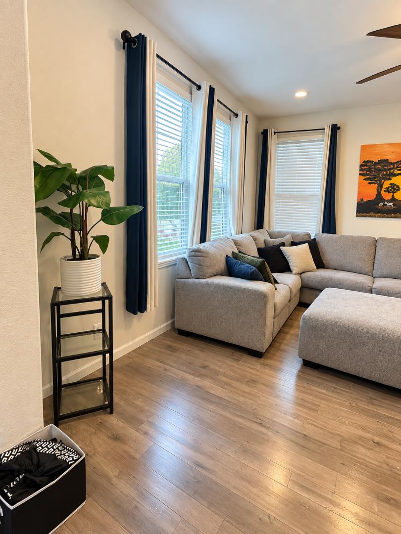 Living room with a gray sectional sofa, tall curtained windows, and wood-look flooring.