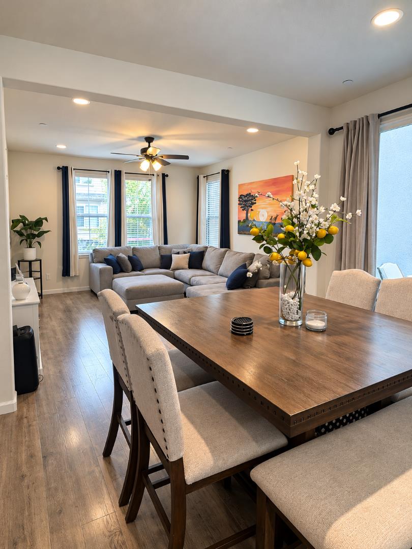 Open-plan dining and living room with a wooden table, gray sectional, and tall windows.