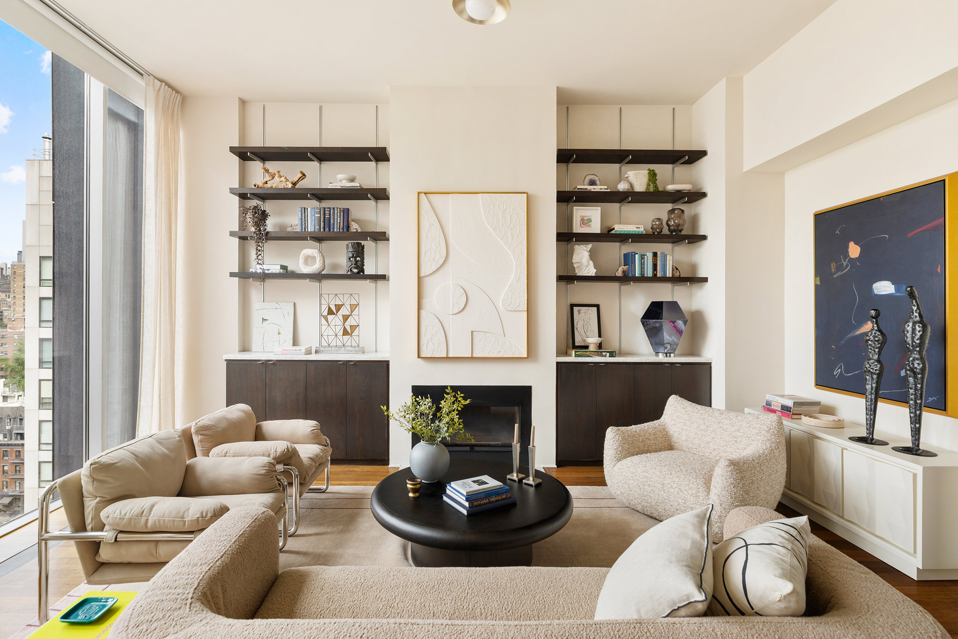 Living room with floor-to-ceiling city-view windows, built-in shelves, a fireplace, and neutral seating.