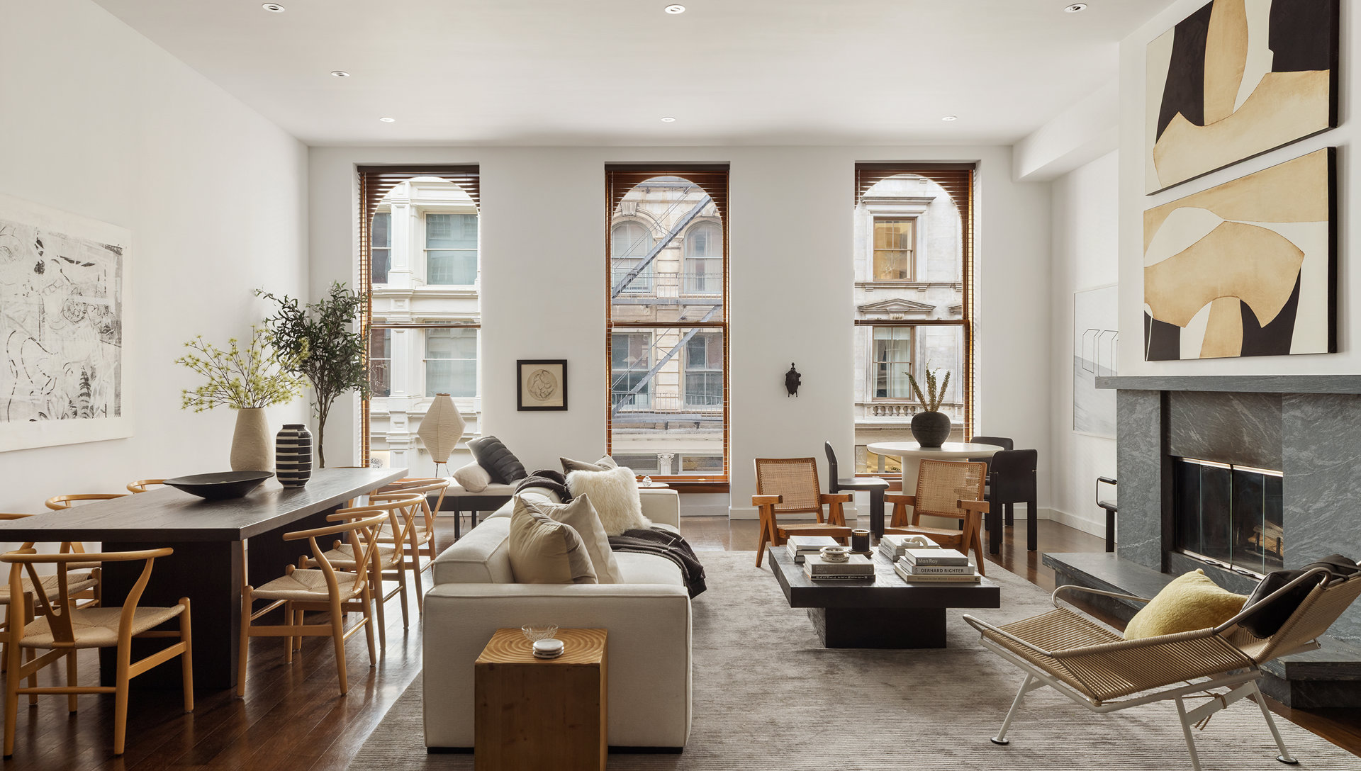 Furnished living and dining room with tall city-facing windows and a marble fireplace.