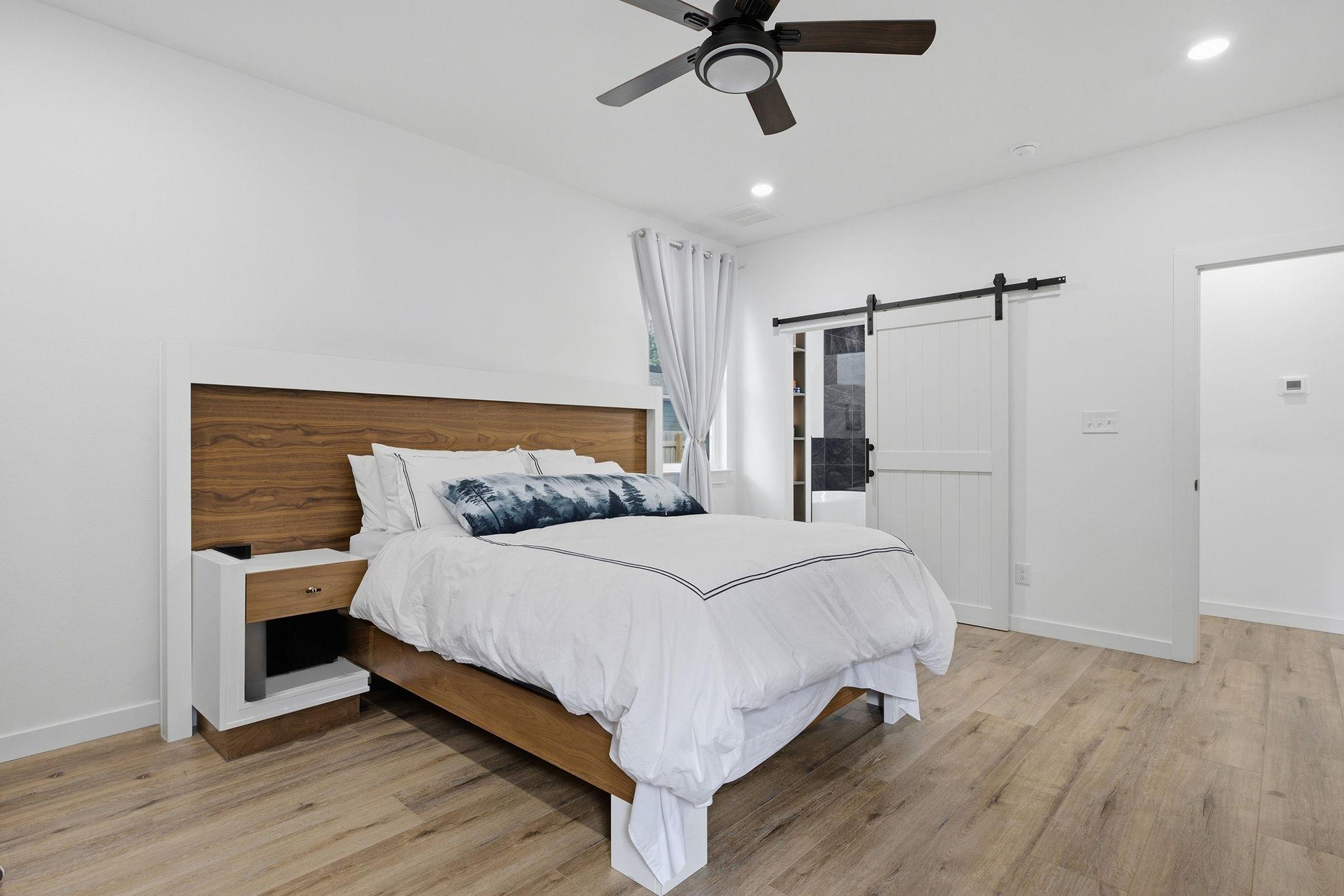 Bedroom with a white bed, wood-paneled headboard, and sliding barn door.
