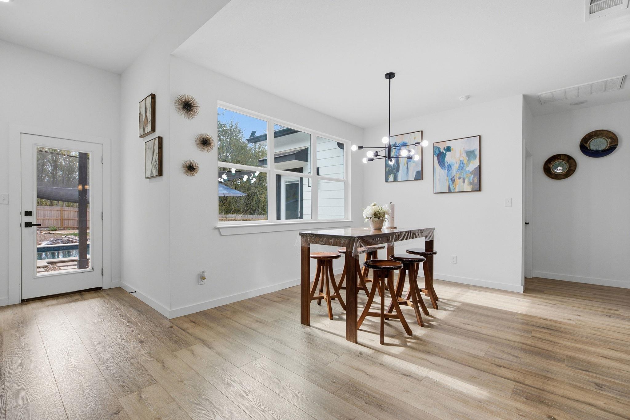 Dining area with a dark wood table, modern chandelier, large windows, and light wood flooring.