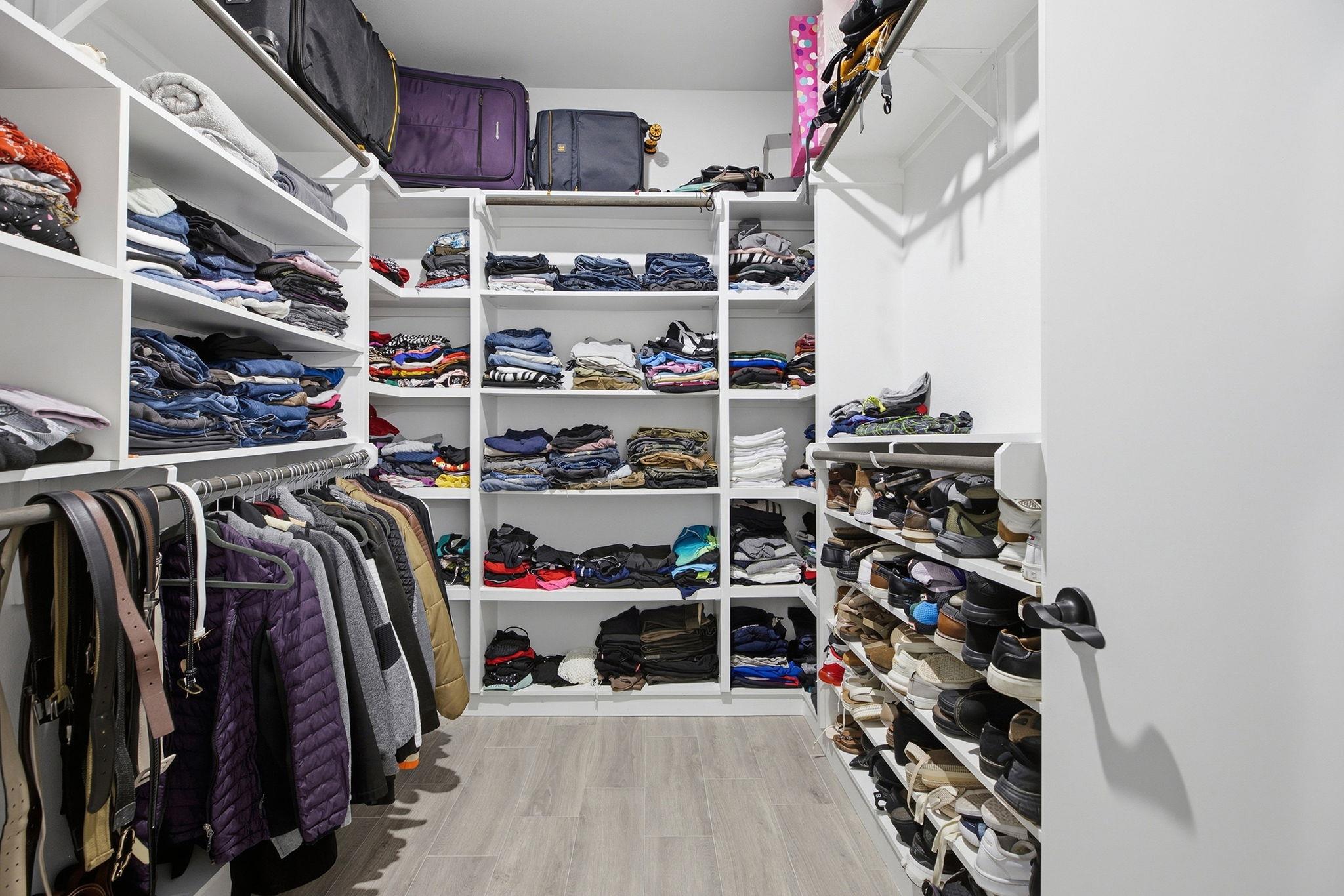 Walk-in closet with extensive white shelving, hanging jackets, folded clothing, and rows of shoes.