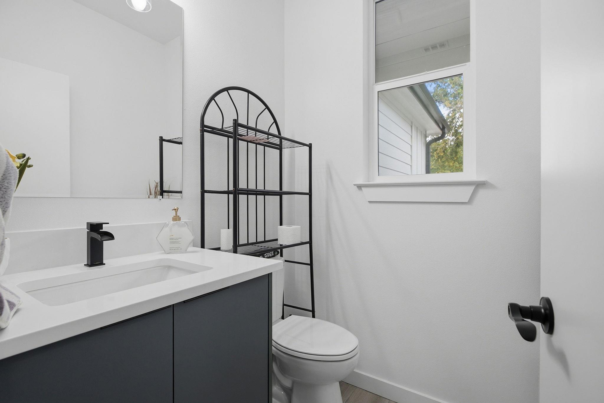 Bathroom with a dark vanity, white sink, black faucet, and toilet beneath a tall window.