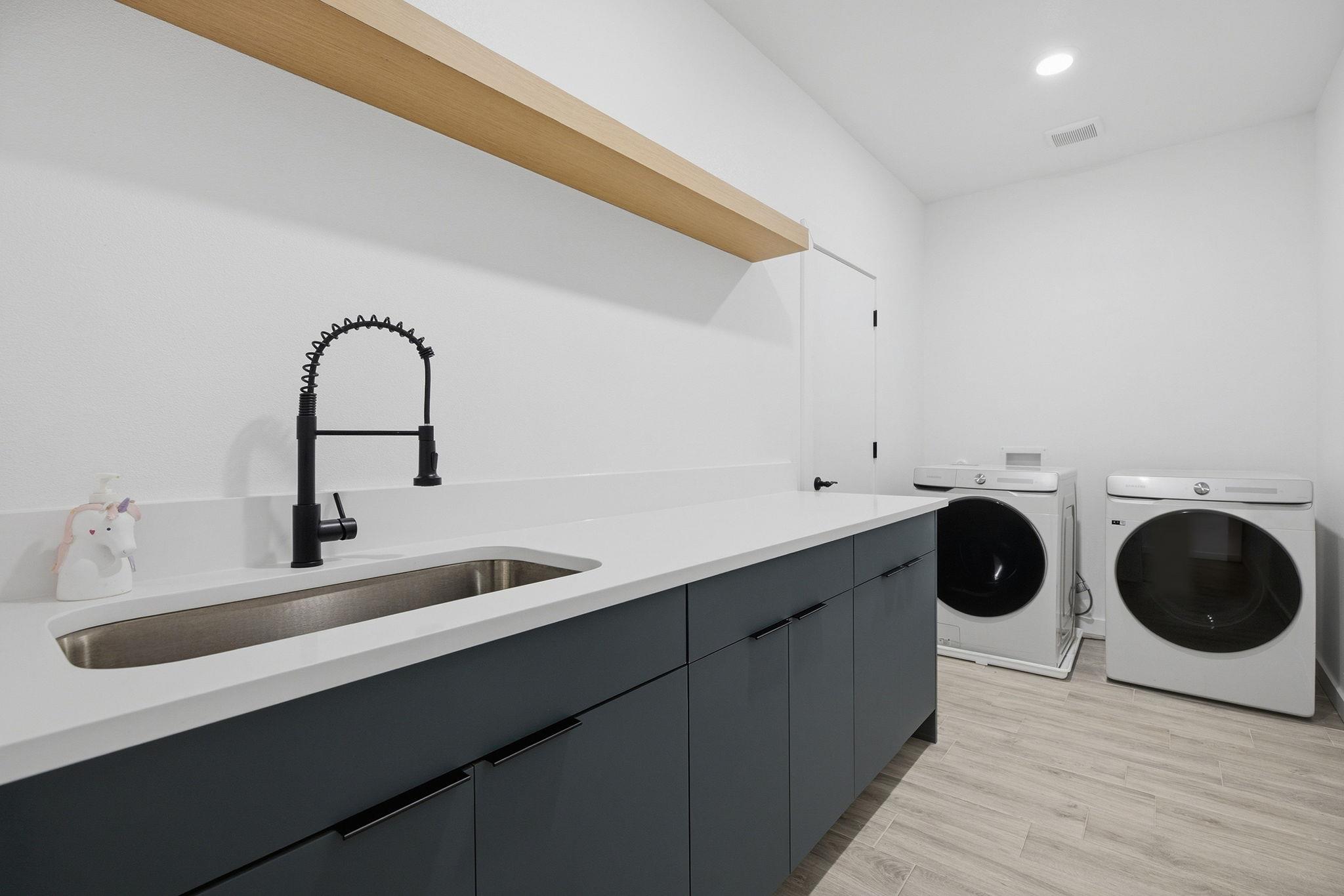Laundry room with a long sink counter, dark cabinets, and side-by-side front-loading washer and dryer.