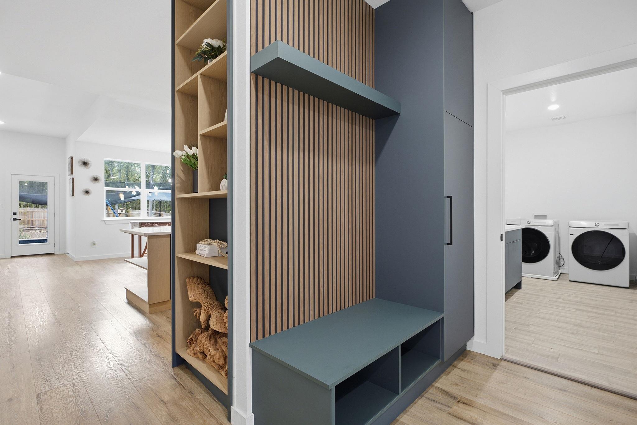 Entryway with a built-in slatted mudroom bench and laundry room beyond.