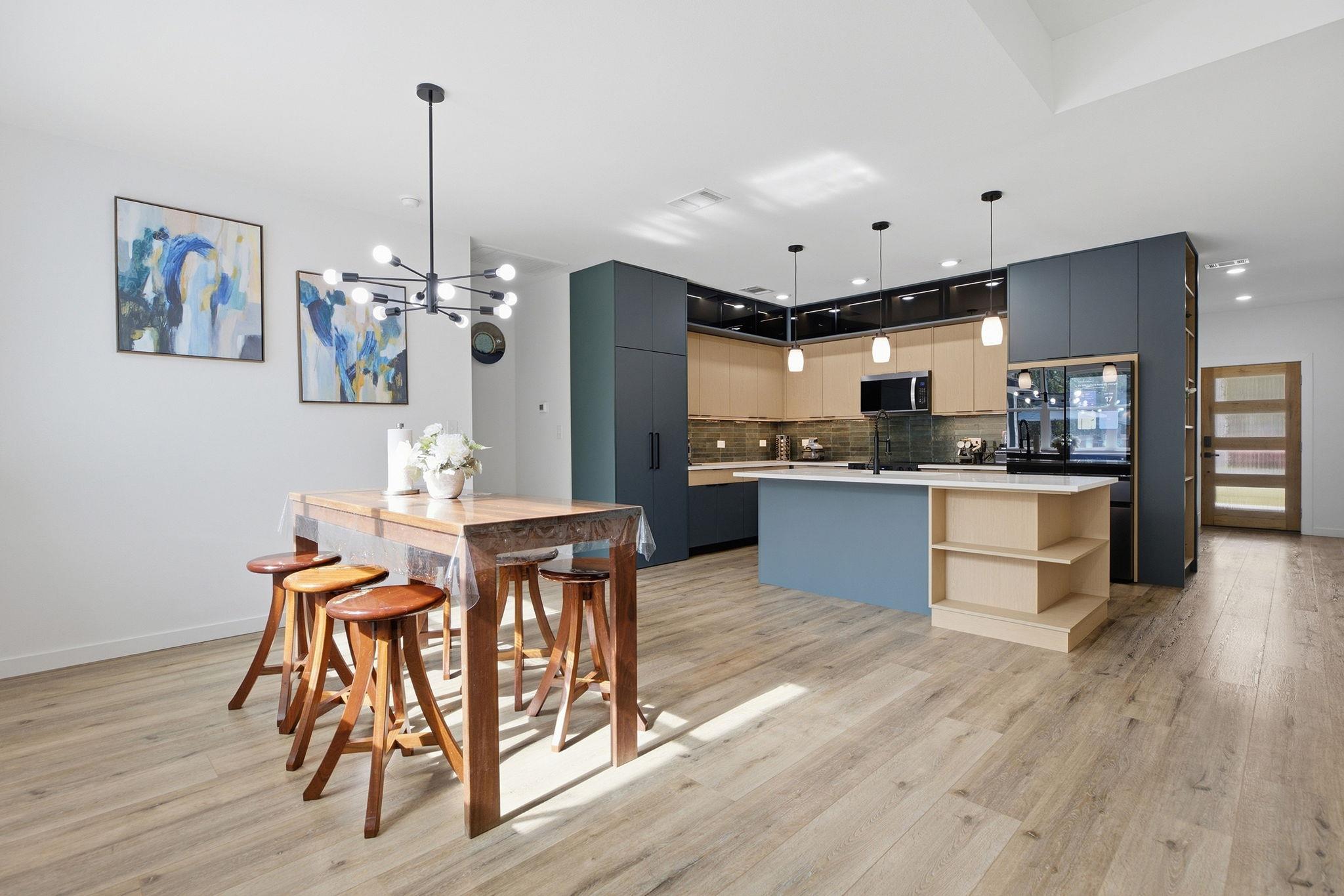 Open-plan kitchen with a large island and adjoining wooden dining table beneath modern pendant lights.