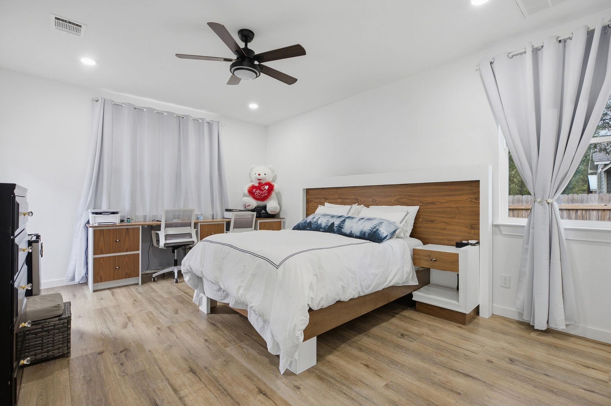 Bedroom with a white bed, wood-paneled headboard, built-in desk, and white curtains.