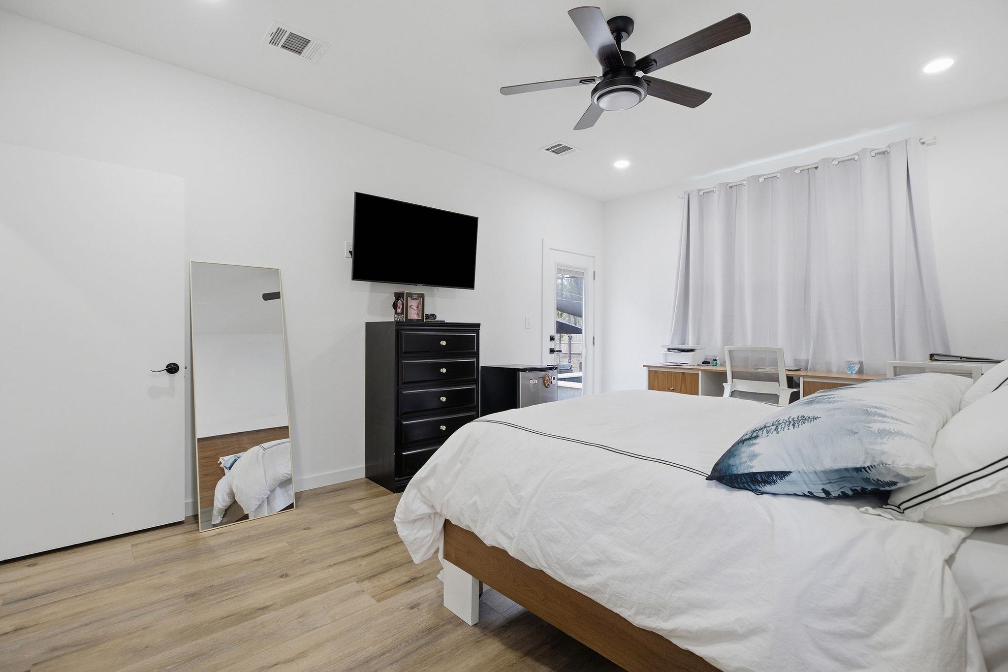 Bedroom with a large white bed, blue accent pillows, a wall-mounted television, and a ceiling fan.