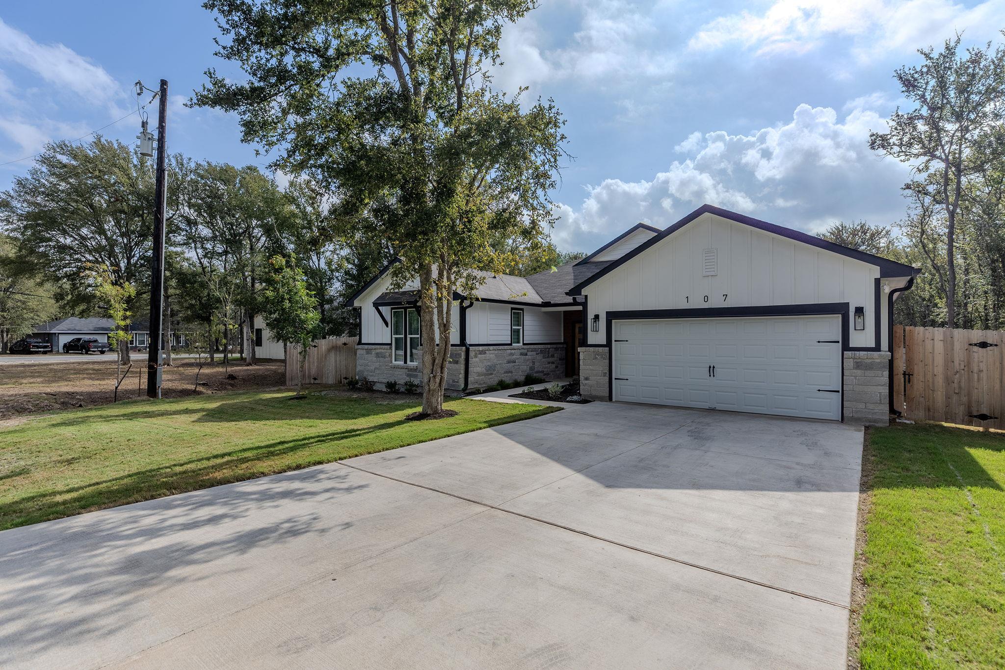 Single-story white house with a stone facade, two-car garage, and broad concrete driveway.
