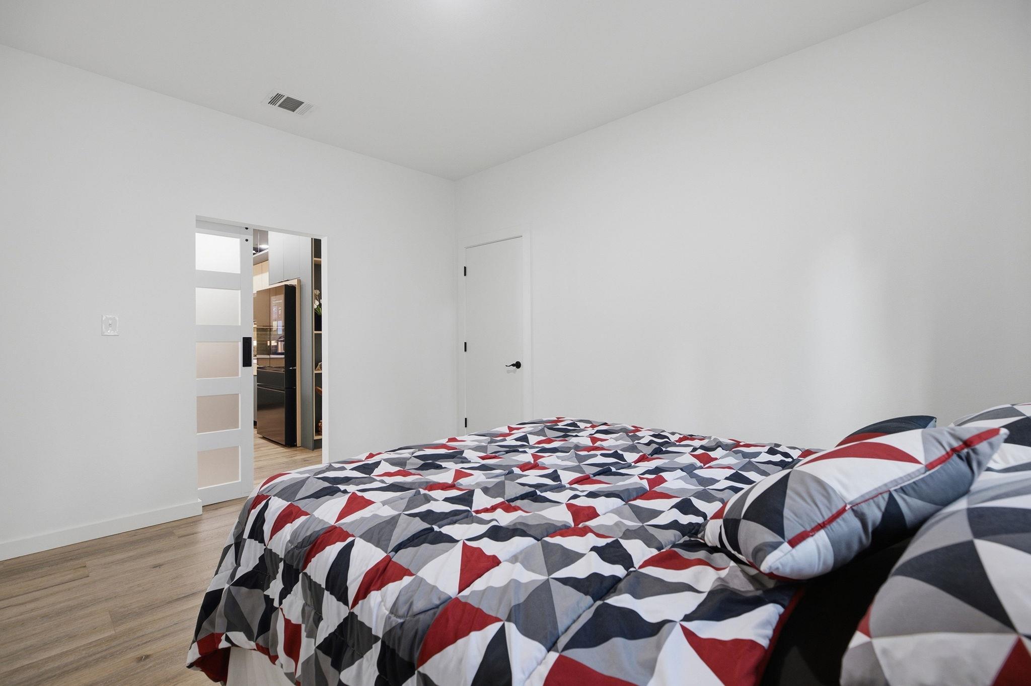 Bedroom with geometric red, gray, black, and white bedding and an open doorway to the kitchen.